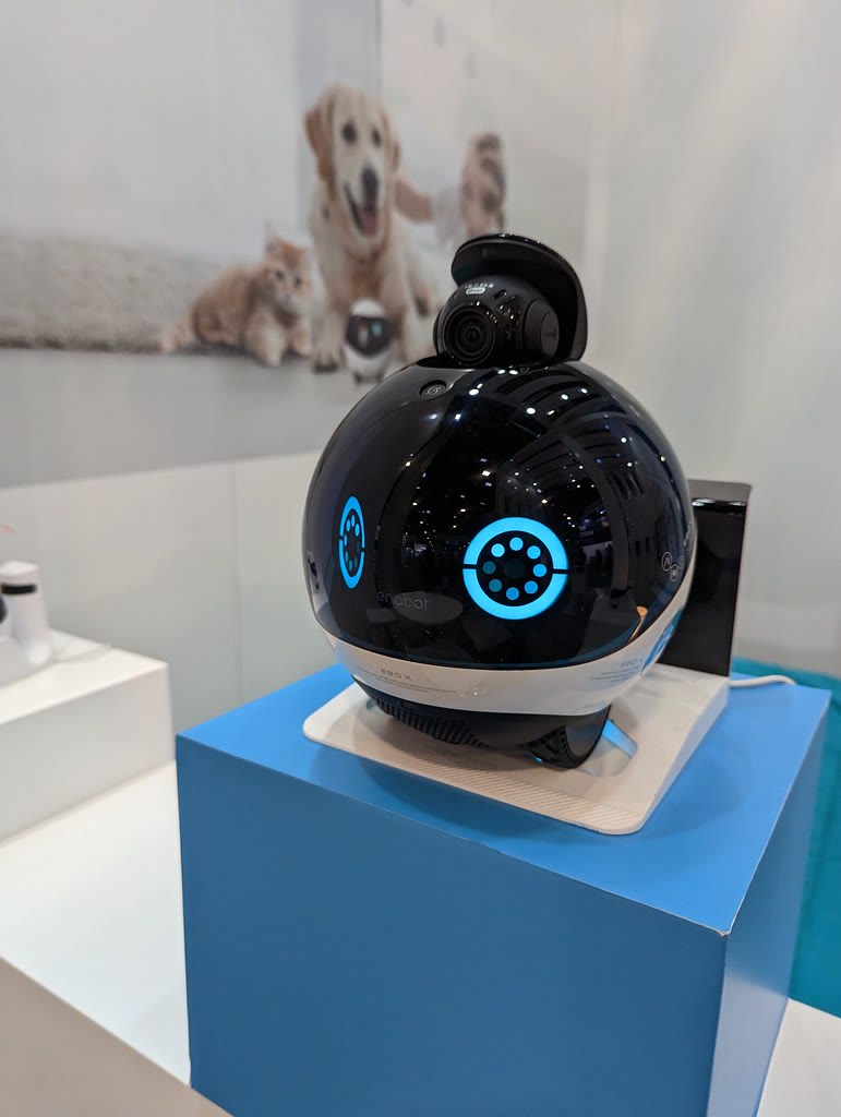 A black and white Enabot EBO X wheeled home robot with its camera raised at a CES display